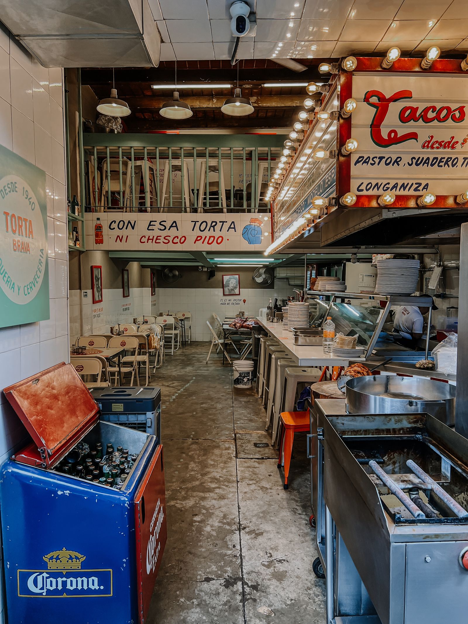 Interior de una taquería con barra, mesas y letrero de tacos